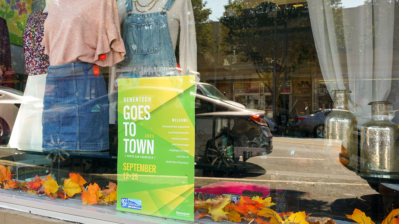 A local store displays a Genentech Goes to Town 2022 poster in the window.
